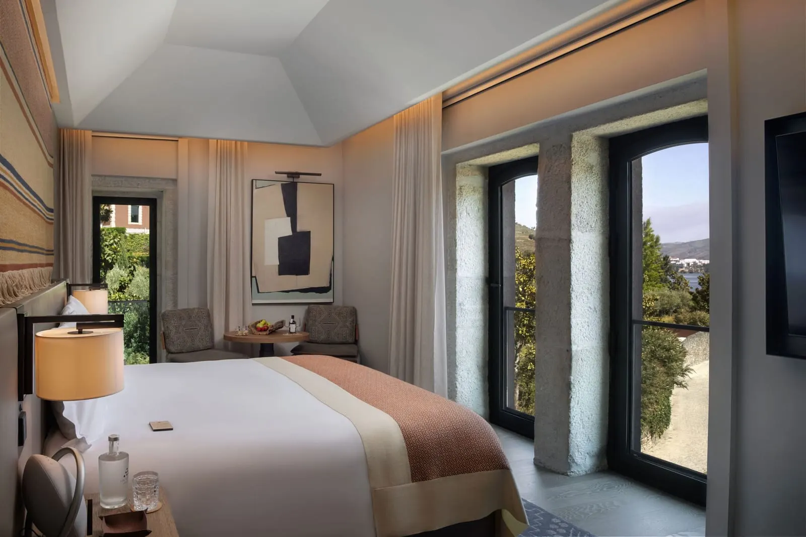 Valley Deluxe at Six Senses Douro Valley: the bed, two armchairs and tall stone-framed windows onto trees