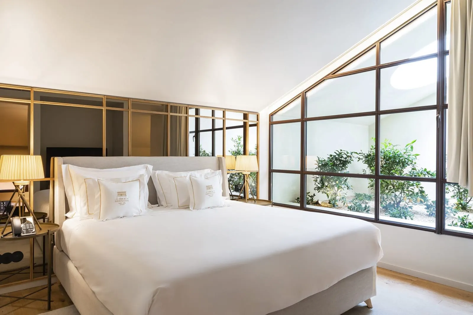 King Premium room at Casa da Companhia: the bed by a brass-framed mirror wall and tall windows onto an inner garden