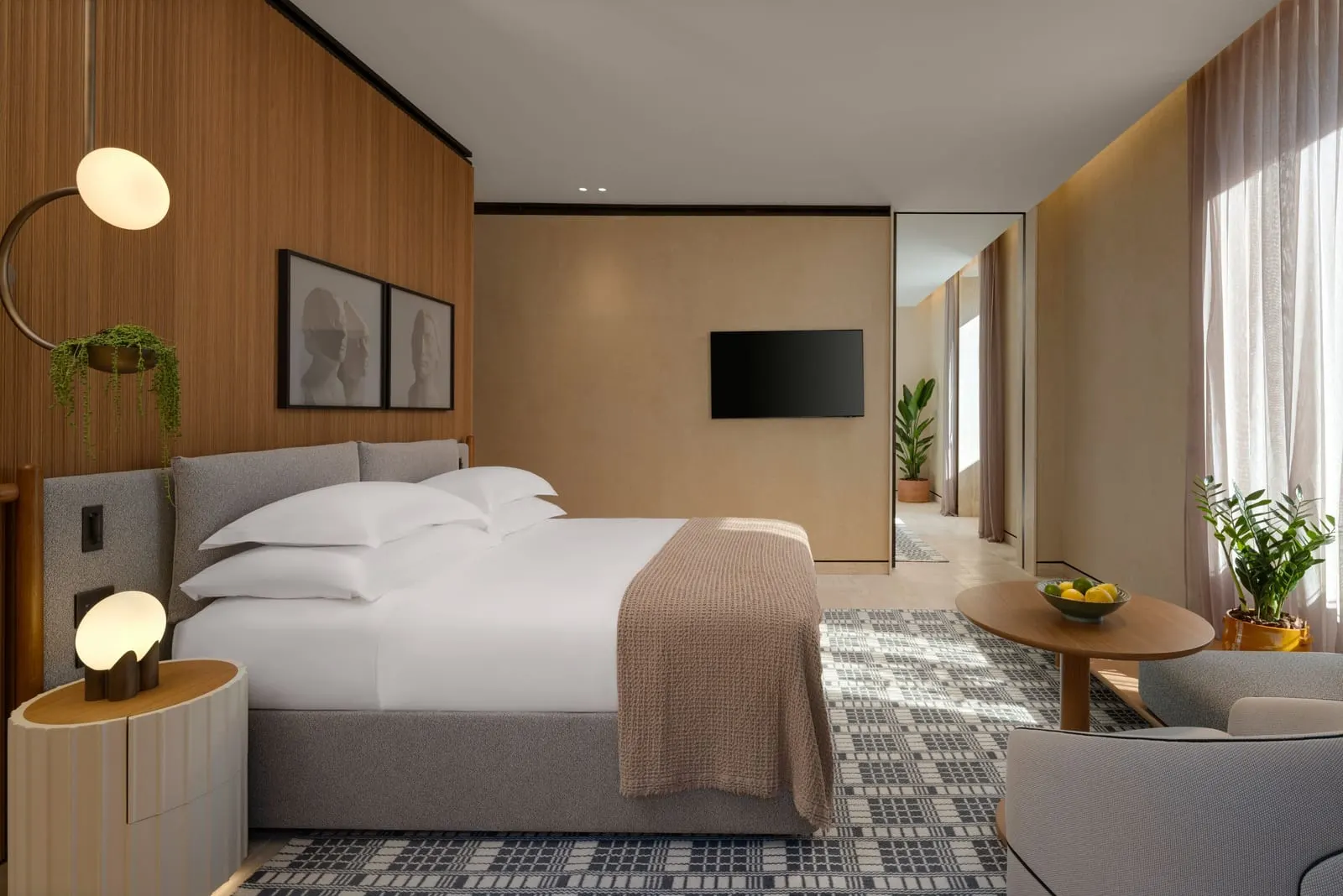 Corner Suite at Six Senses Rome: the bed, a round table and an armchair, with a TV and a corridor beyond