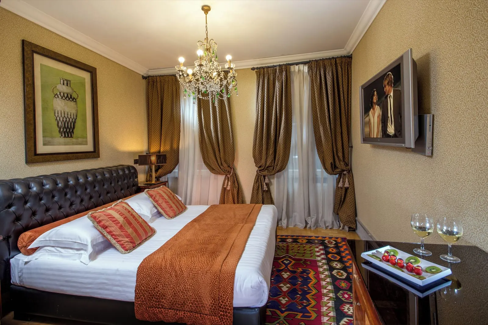 Superior Double Room at The Inn at the Roman Forum: a bed with a tufted leather headboard, a patterned rug and a chandelier