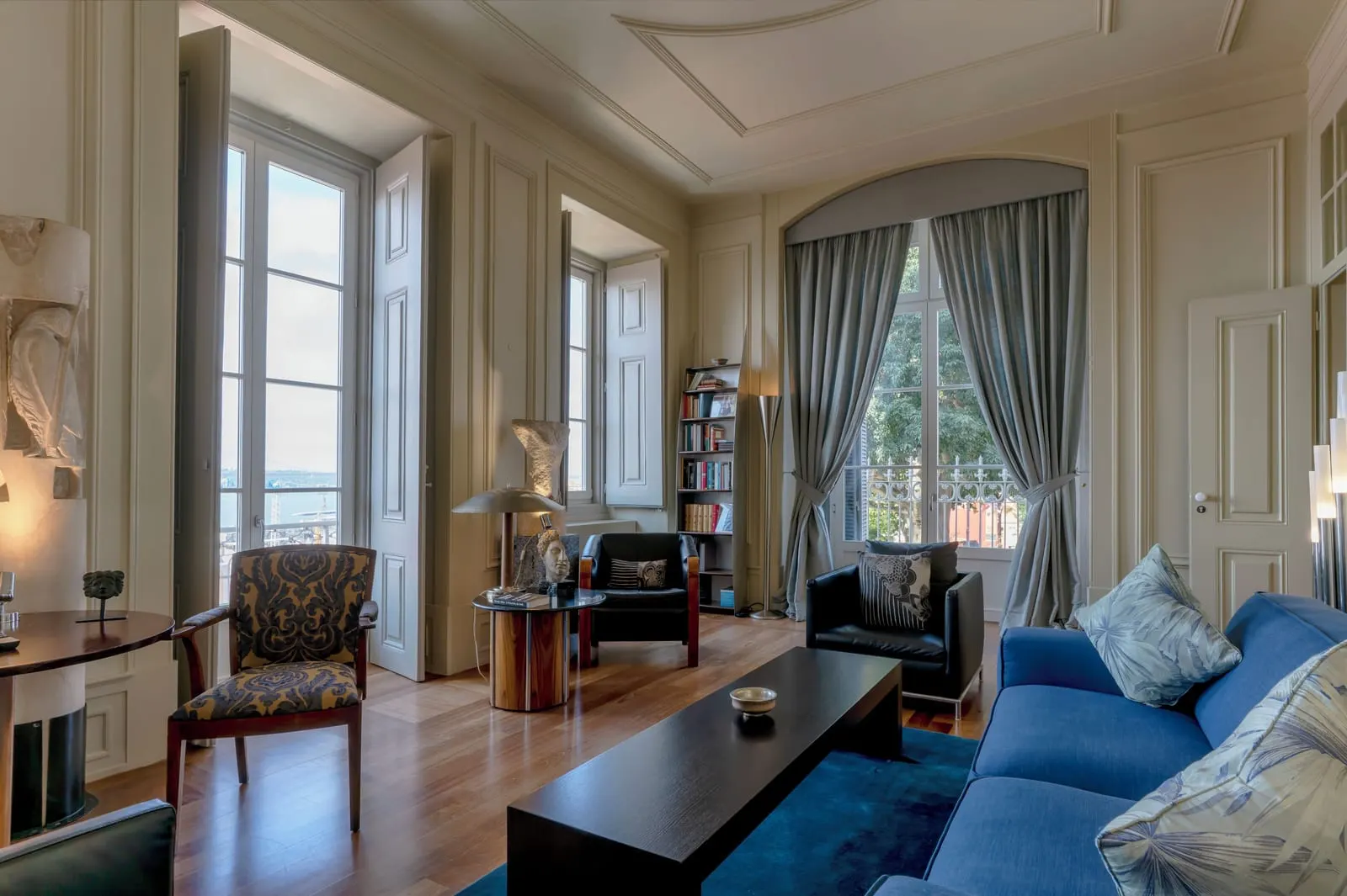 Salavisa Suite at Verride Palácio Santa Catarina: the sitting room with a blue sofa, armchairs, bookshelves and tall windows