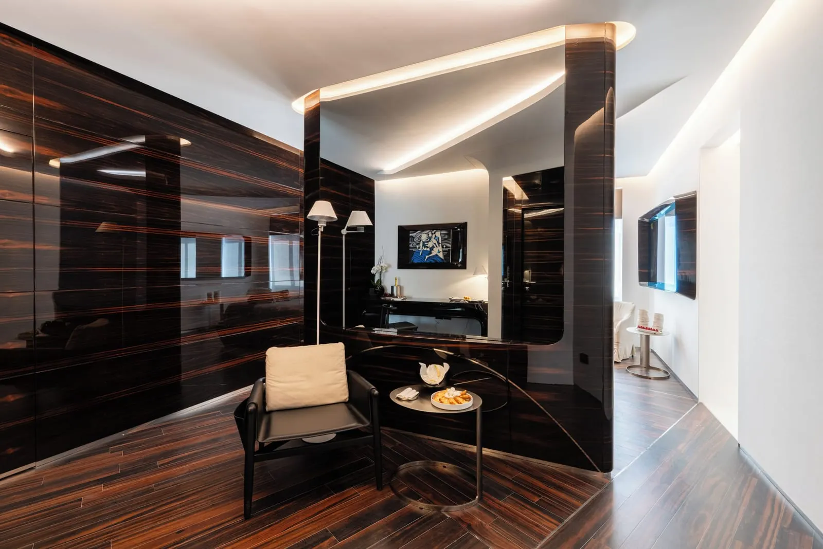 Junior Suite at ROMEO Roma: an armchair and a small table beside a curved ebony partition, with a desk beyond