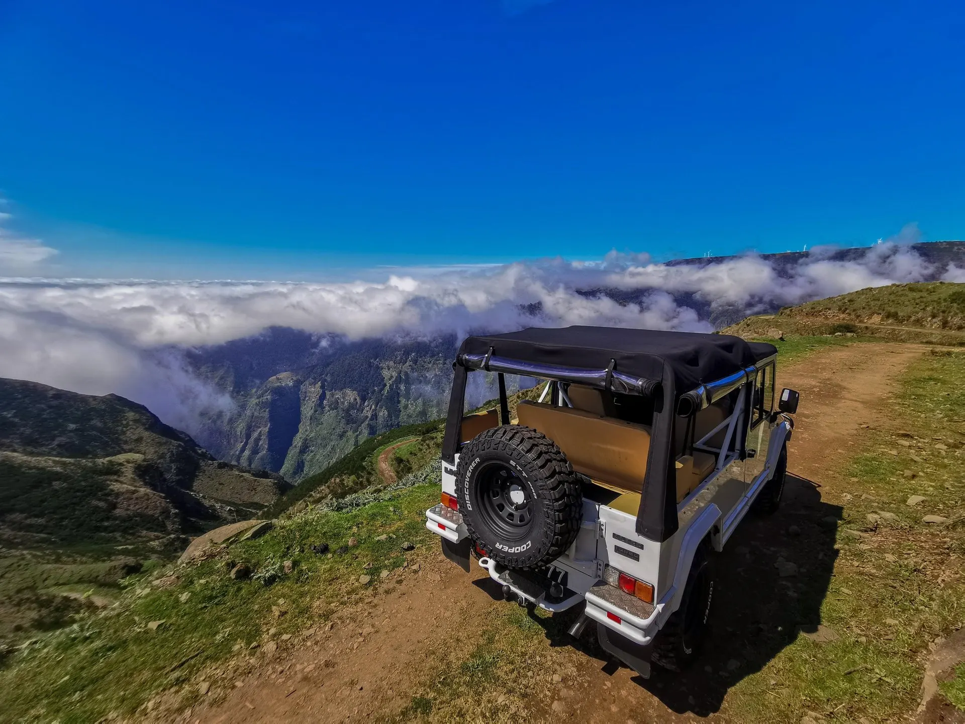 A white open-topped 4x4 parked on a dirt track at the edge of the plateau, looking down into a green valley with cloud below