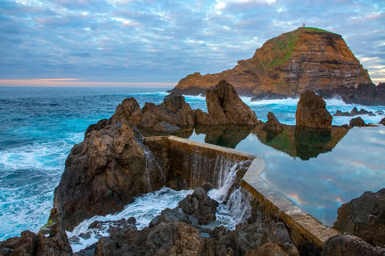 The natural lava pools at Porto Moniz, with Atlantic waves spilling over the rocks and the islet and its lighthouse behind